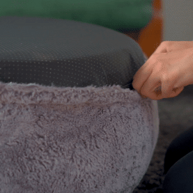 Hand adjusting a soft, fluffy cover on a round cushion.