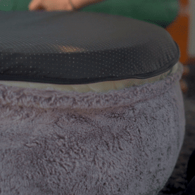 A person unzipping the cover of a deep purple, fluffy bean bag chair.